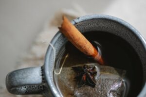 Photo taken from above of a cup of tea containing a floating teabag, star anise and a cinnamon stick