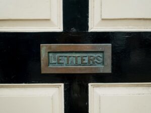 Close up of a black and white front door with a tarnished brass letterbox
