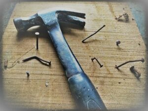 Black claw hammer on brown wooden plank with crooked nails