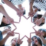 A circle of people forming a star shape with their fingers.