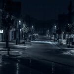 Black and white photo of a deserted town street in the dark lit by streetlights