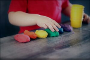 Soft skills training courses - photo of a person standing at a table with 6 different coloured pieces of modelling dough in front of them