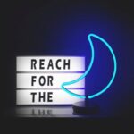 A sign with the words Reach for the, beside a blue neon illuminated light in the shape of a crescent moon.