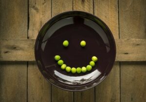 A brown ceramic plate with a smiley face made out of green peas.