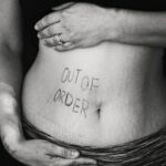 Black & white photo of someone's midriff with the words "out of order" written across their stomach