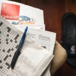 A small fan of newspapers with the word opinion showing and an unfinished crossword with a pen lying open on top of the pile