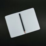 A notebook opened on two blank white pages with a pencil lying on the centre spine
