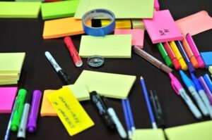 An assortment of sticky notes and pens mixed up on a table-top for health in the workplace resources in Spring newsletter