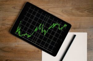 A rising upward graph on an ipad screen resting on a desktop with a blank piece of paper and pencil beside it