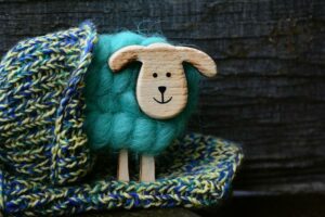 Some blue and yellow hand knitting with a small wooden sheep with a turquoise woollen fleece popping out