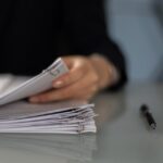 Close up photo of a person holding the top item from a pile of paper-clipped paperwork