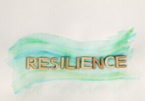 The word resilience made with wooden letters against a cream background with an abstract wave of green hues across it